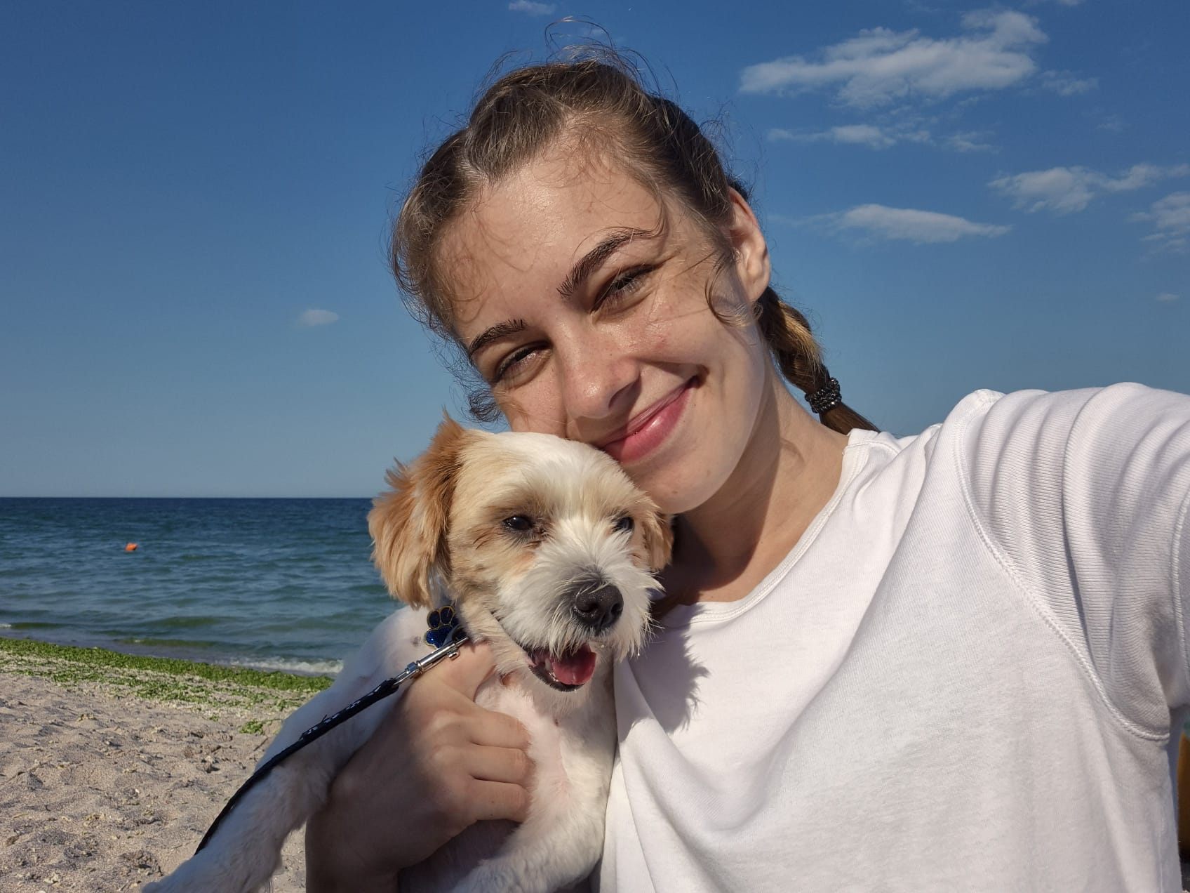 Groomerul zâmbește pe plajă ținând un cățel în brațe